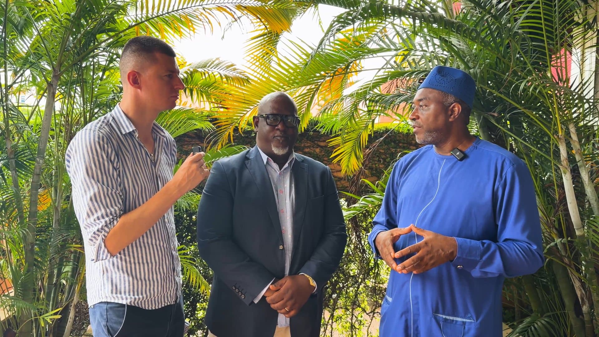 Ladislas Maurice in conversation with two executive members of the Inter-Religious Council of Sierra Leone, standing outdoors among palm trees.