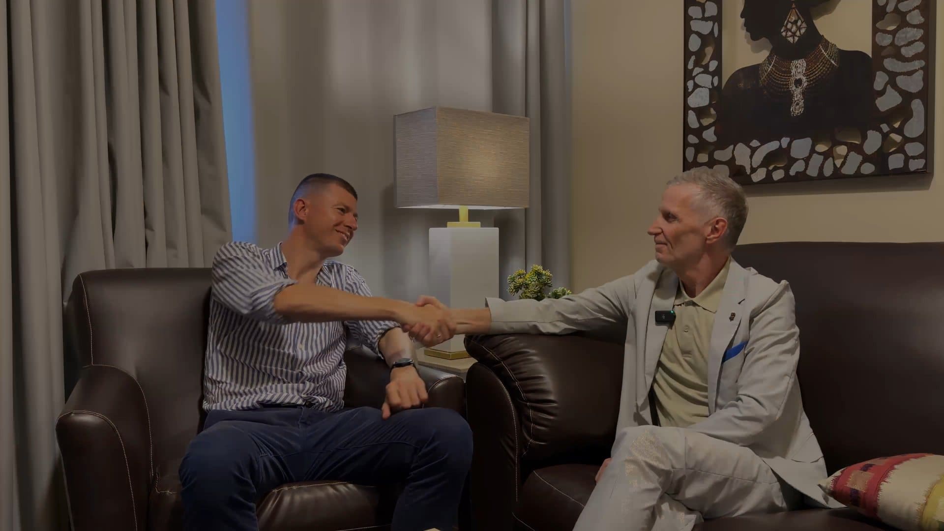 Ladislas Maurice and Stephen Barnes shaking hands while seated on leather sofas during an interview in Freetown.