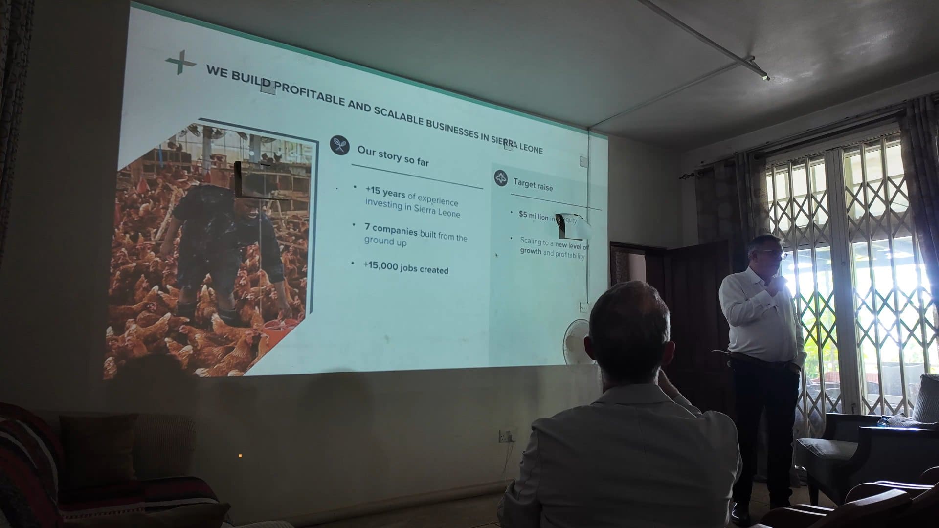 A Truestone presentation projected in a Freetown meeting room, with a slide titled We build profitable and scalable businesses in Sierra Leone and a photo of a poultry farm.